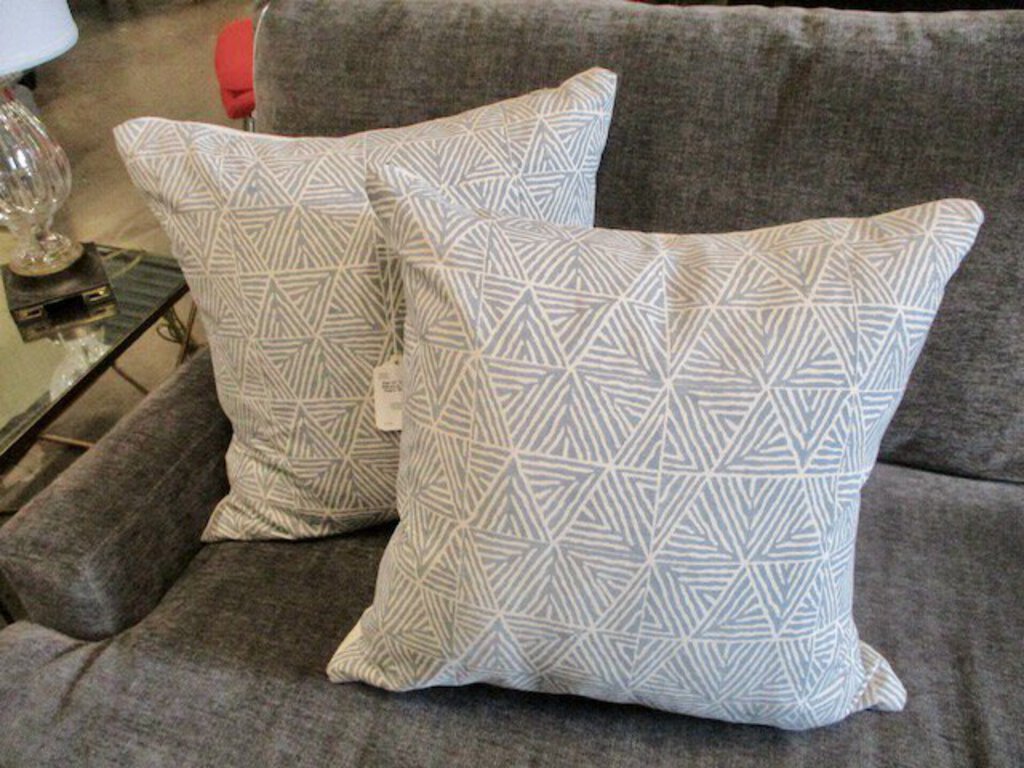 Two decorative throw pillows with blue and white geometric triangle patterns on a gray sofa