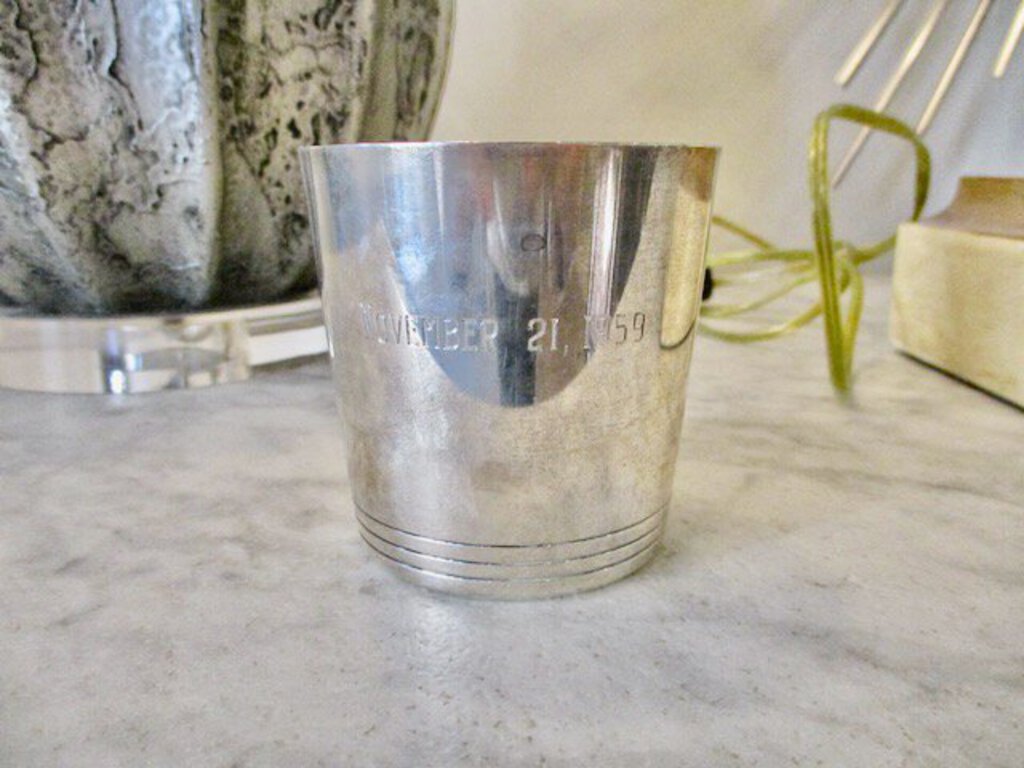Silver metal cup with engraved date November 21, 1959 on marble surface with decor