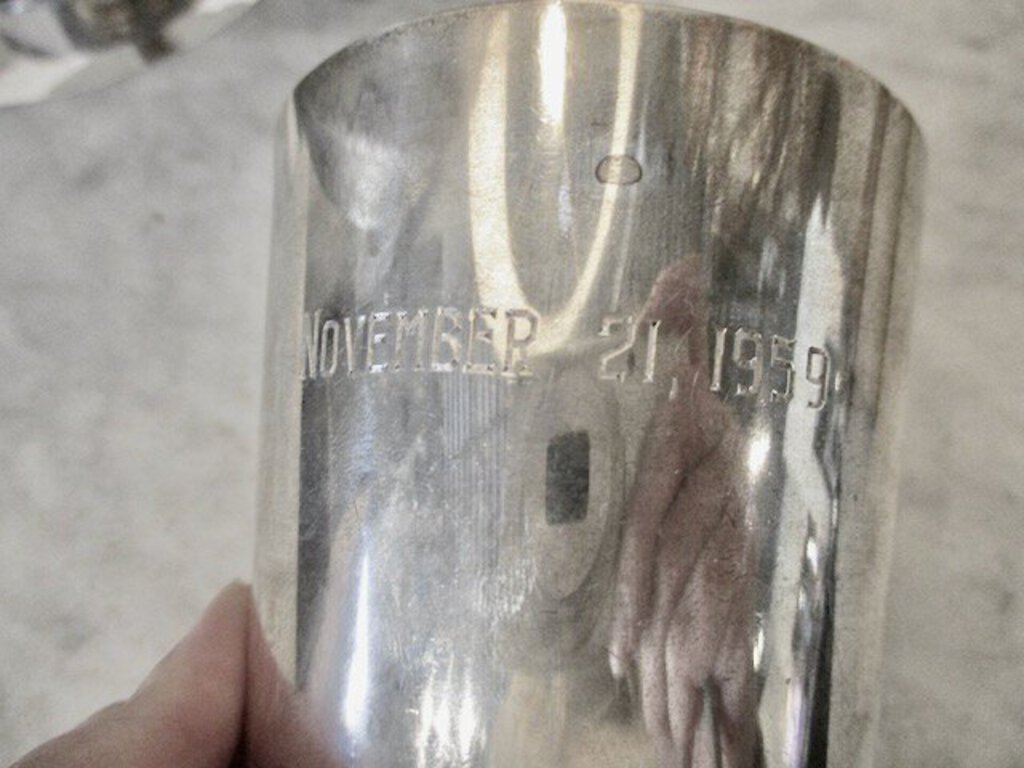 Close-up of a reflective silver cup engraved with the date November 21, 1959