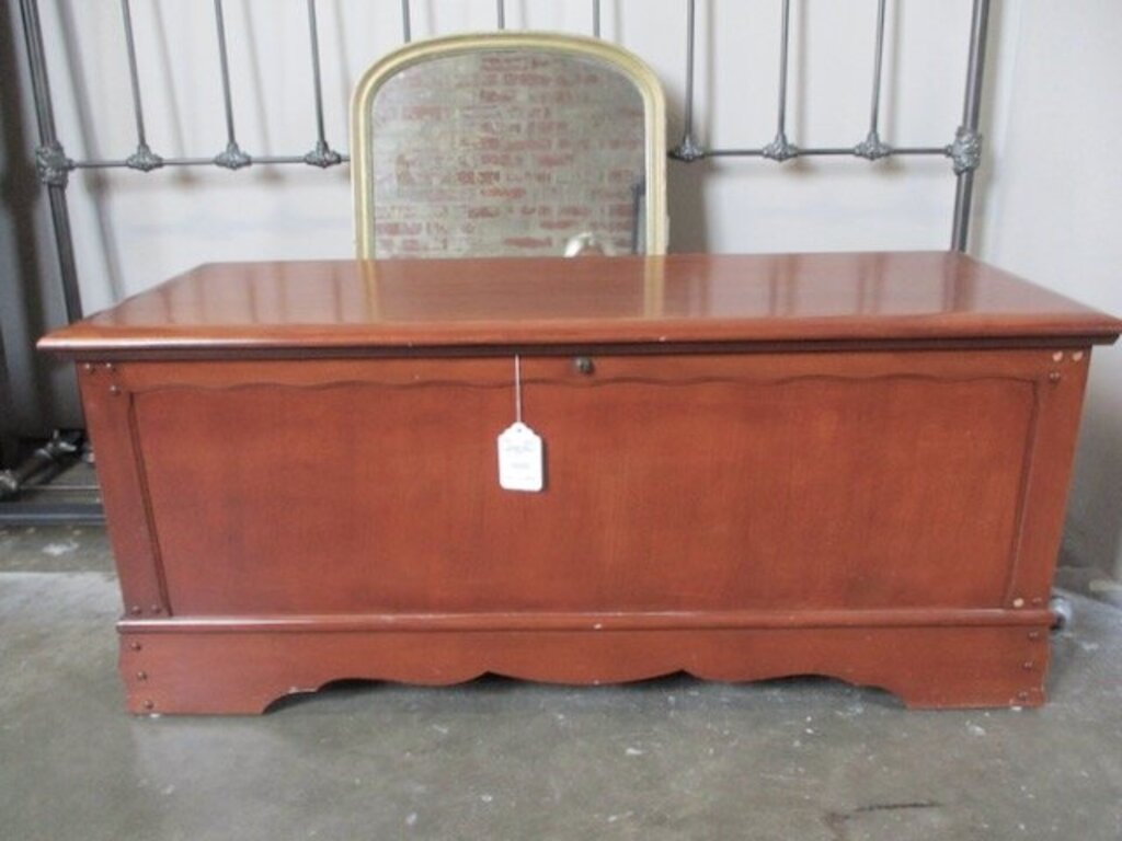 Vintage wooden blanket chest with scalloped base and key lock detail sitting on concrete floor