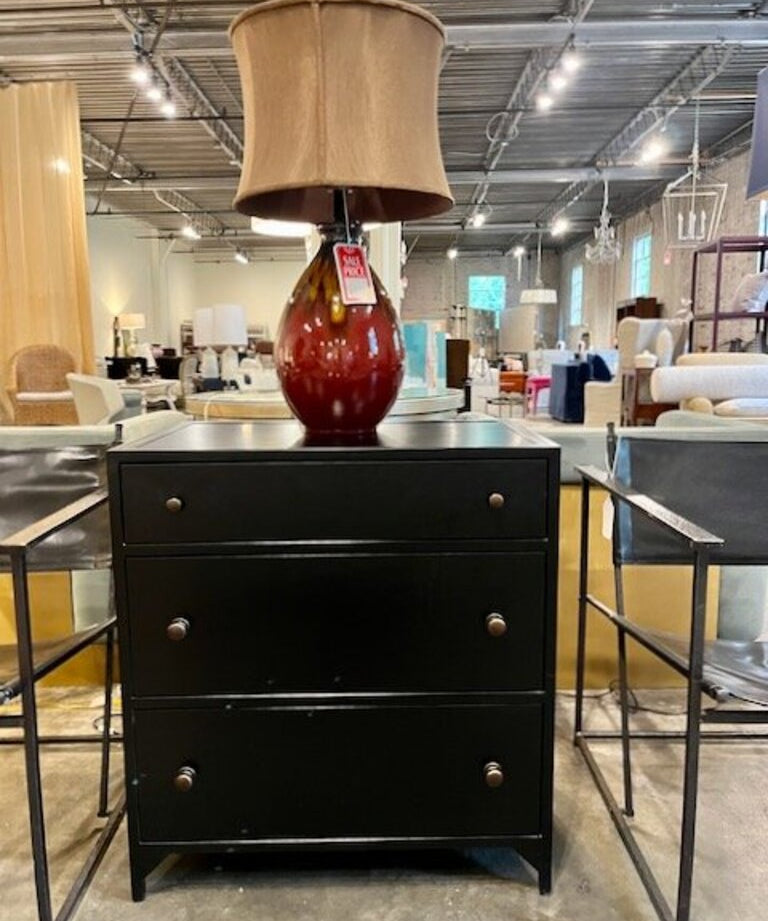 Black three-drawer dresser with brown table lamp and beige lampshade in furniture store